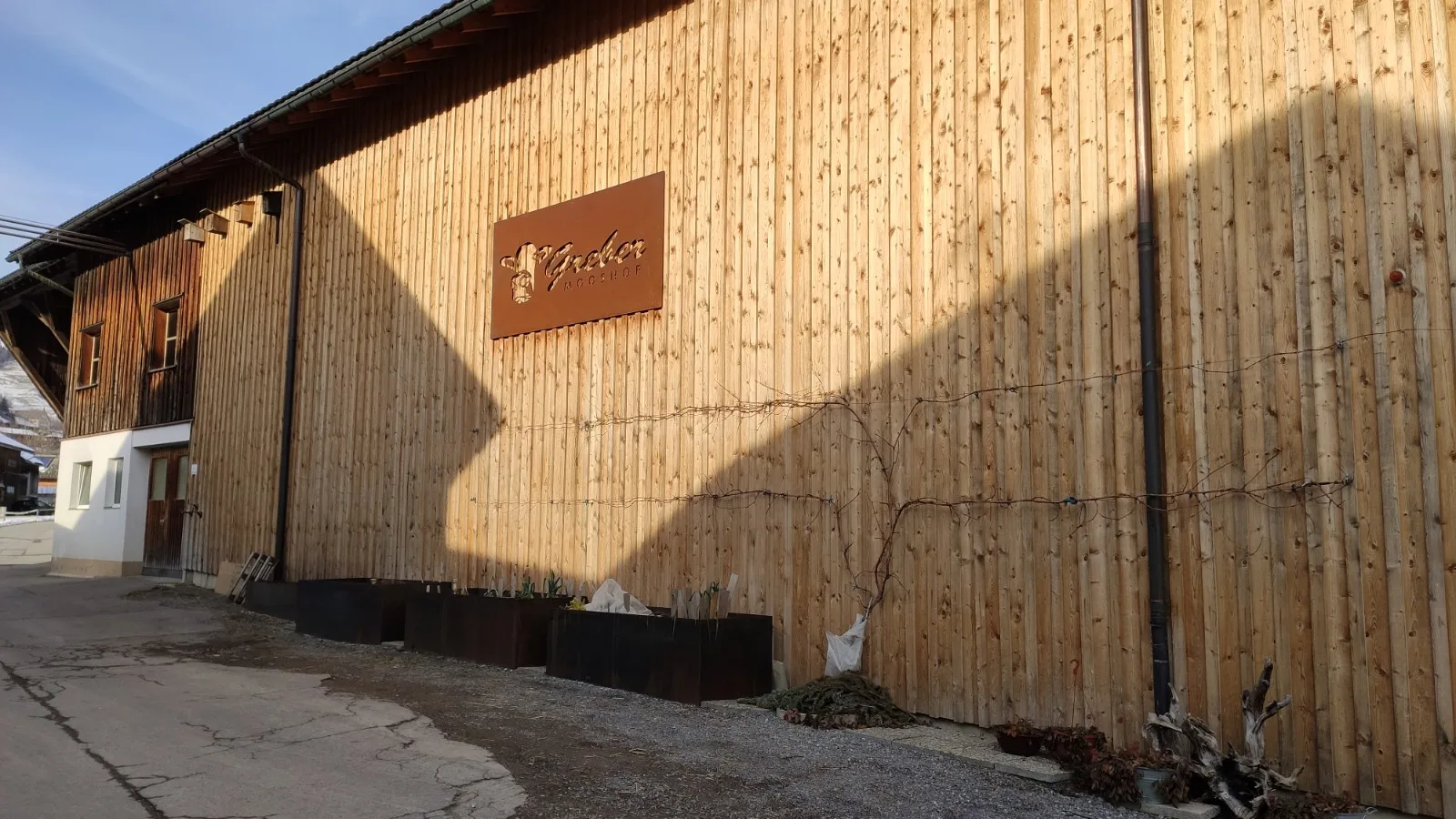 Holzfassade des Hofgebäudes mit dem Corten-Schild Greber Mooshof